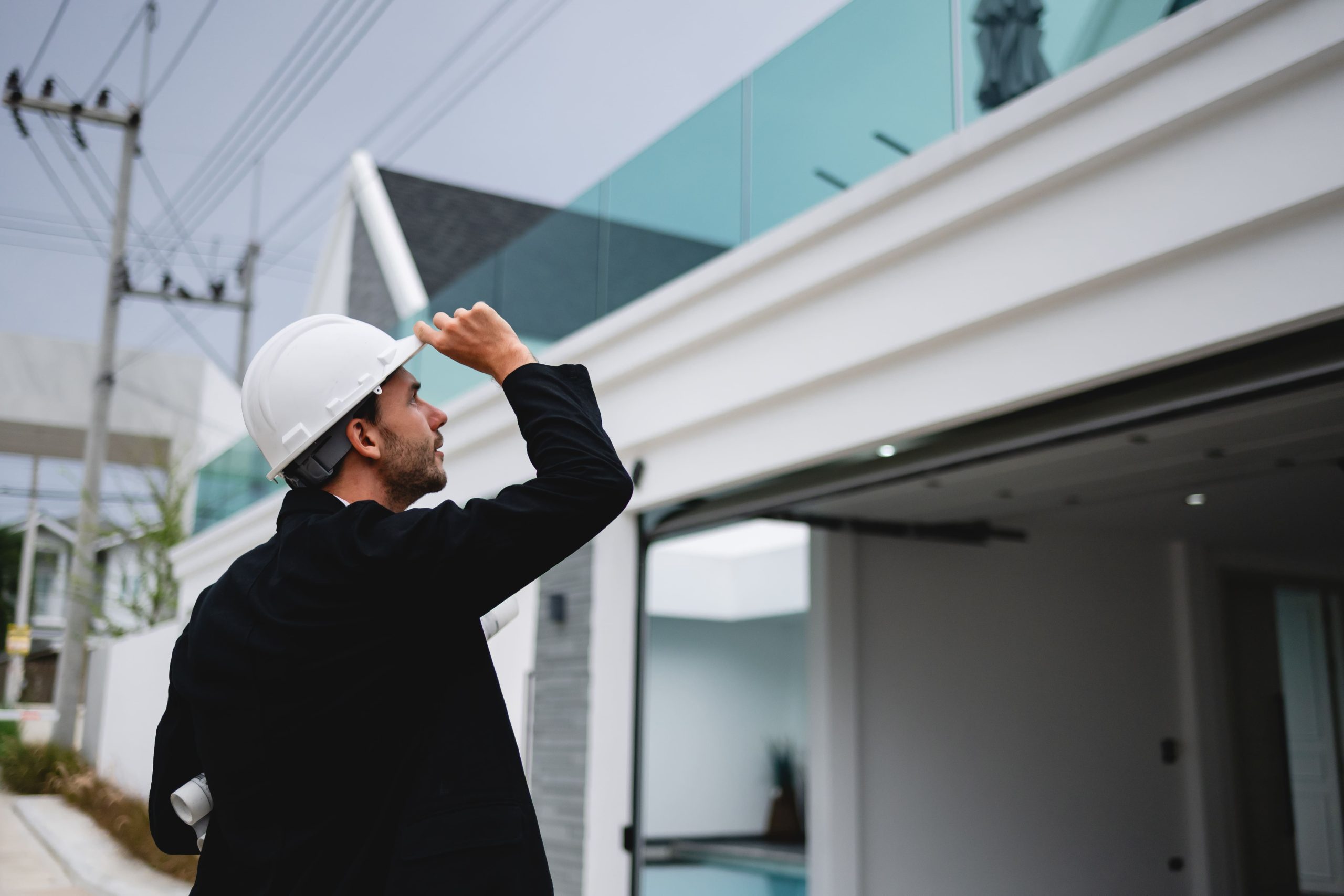 building inspector in a white hard hat looking at the roof of a modern home